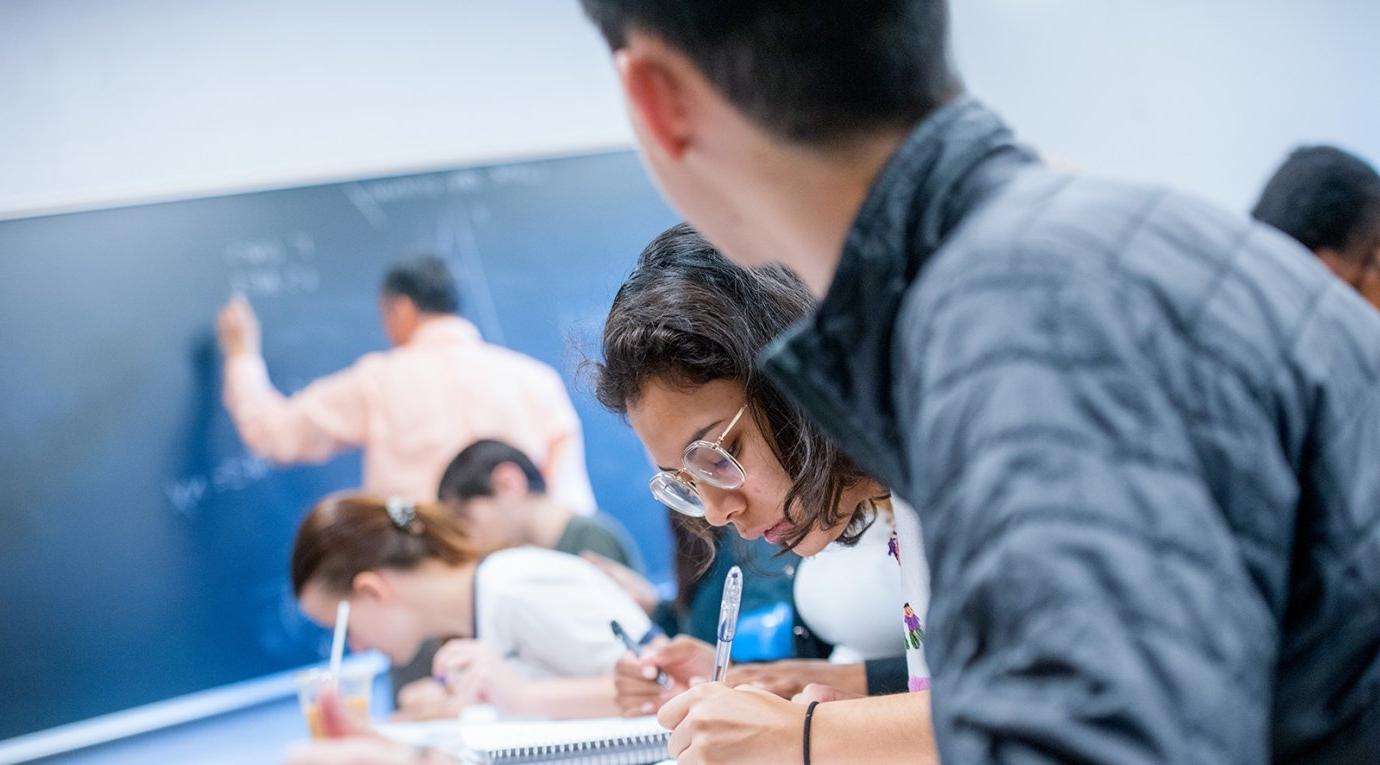 students in class watch the professor write on chalkboard